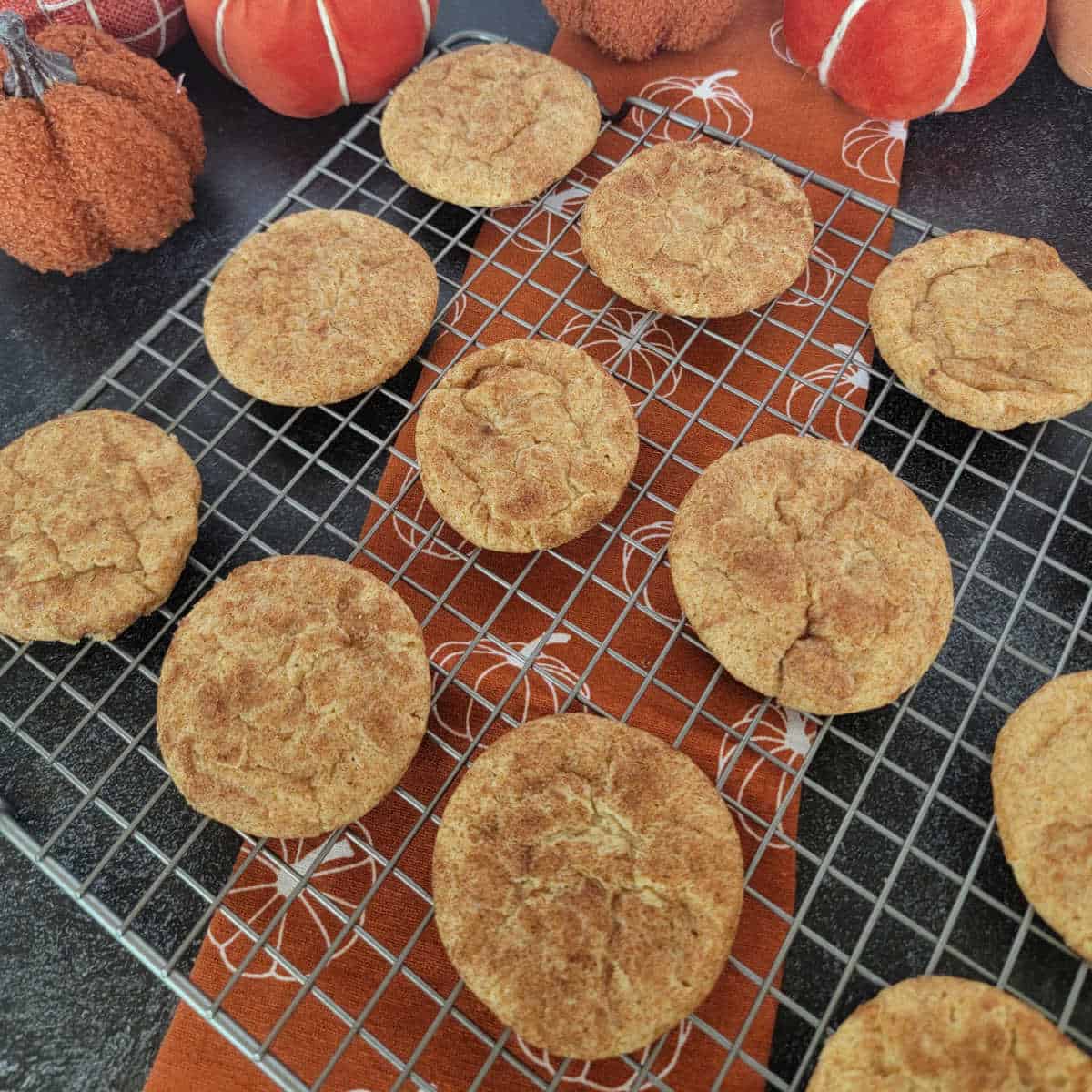 Pumpkin Snickerdoodles on a wire rack over a pumpkin napkin with cloth napkins in the background
