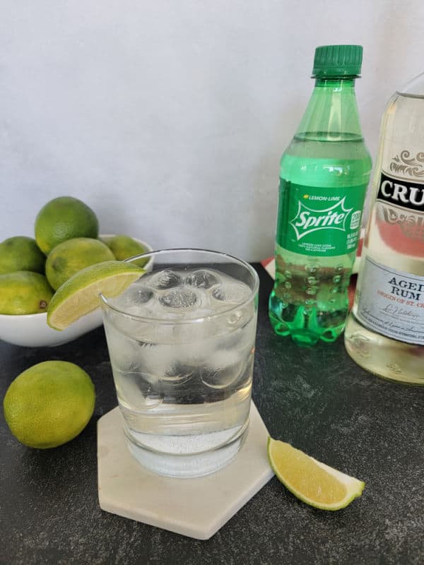 2 ingredient sprite and rum cocktail next to a bowl of limes and a bottle of Sprite