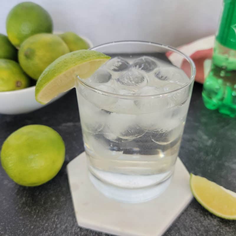 Rum and Sprite Cocktail on a white coaster with a bowl of limes