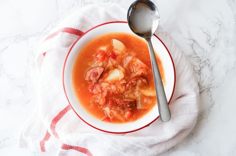 sausage sauerkraut soup in a white bowl with a spoon on it. 