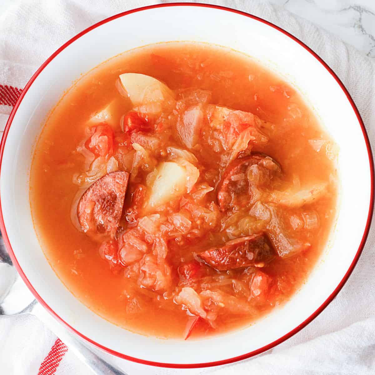 Sausage Sauerkraut Soup in a white bowl on a cloth napkin