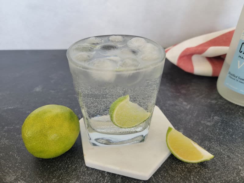 Vodka Sprite Cocktail with a lime wedge on a coaster next to limes