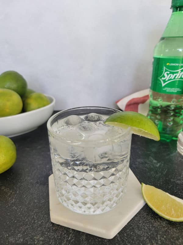 Tequila and Sprite cocktail in a rocks glass next to a bowl of limes and a bottle of Sprite