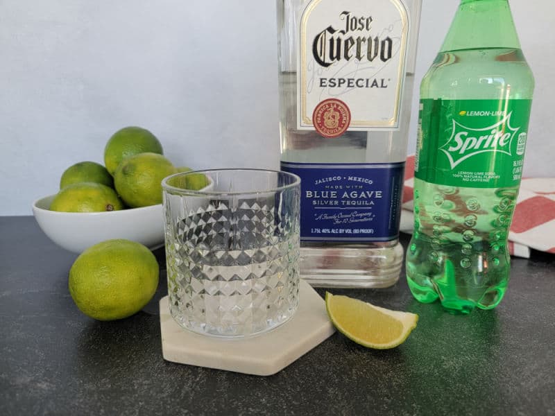 Cocktail glass on a coaster, bowl of limes, Jose Cuervo tequila blue agave and a bottle of sprite
