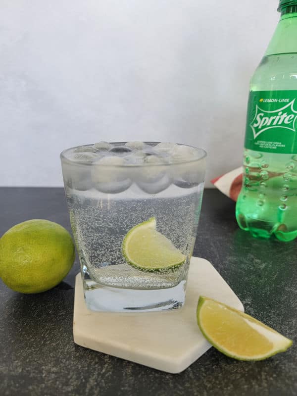 Sprite and vodka cocktail next to a lime, and a bottle of sprite 