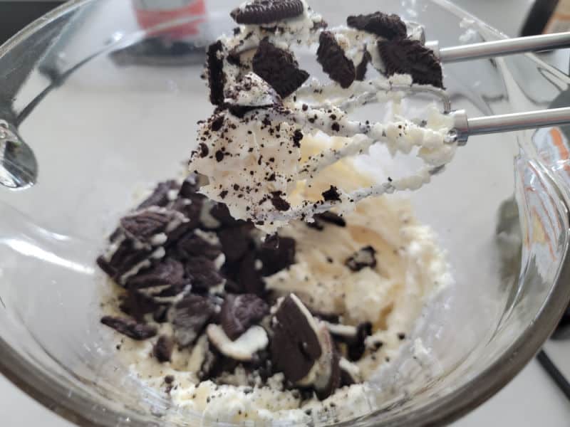 Mixer handles coated in No Bake Oreo Cheesecake above a glass bowl