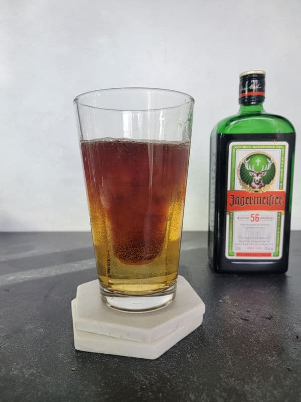 Jager Bomb Cocktail in a tall glass next to a bottle of Jägermeister 