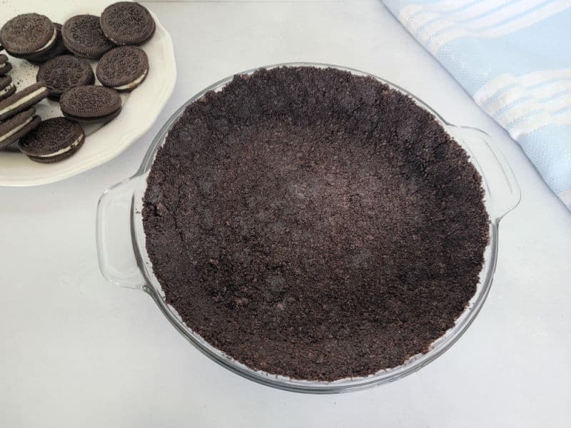 No Bake Oreo Crust in a pie dish next to a plate of Oreos
