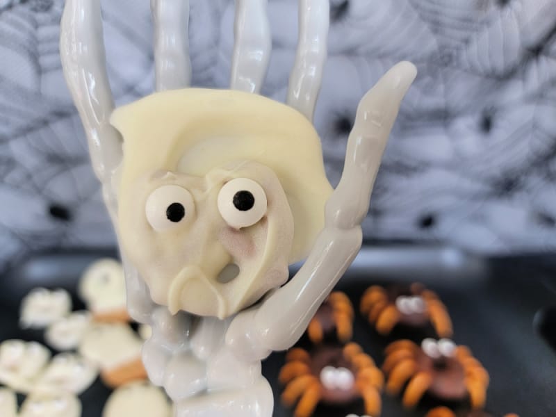 Ghost pretzels with candy eyes held on a skeleton hand