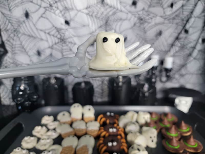 marshmallow ghost on a skeleton hand over a platter of halloween treats