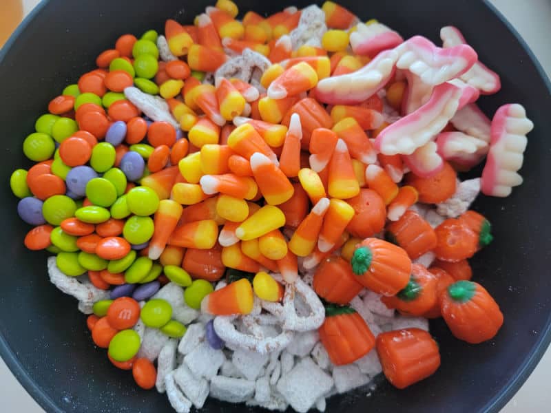Monster munch ingredients in a black bowl M&Ms candy corn chocolate pretzels, gummy fangs