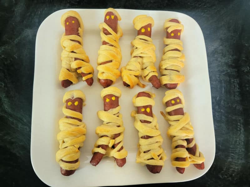 crescent wrapped mummy hot dogs on a white plate