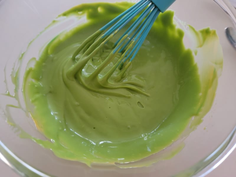 green cheese sauce with a blue whisk in a glass bowl