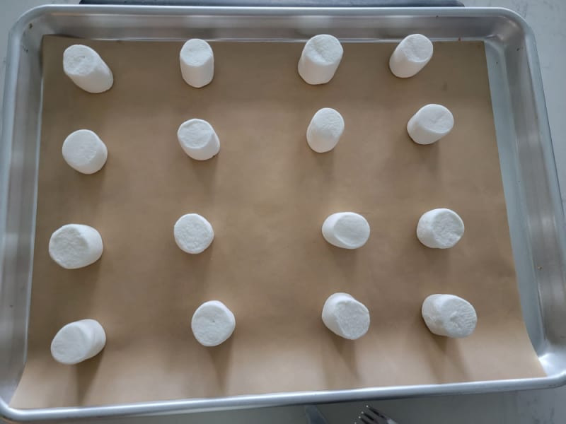marshmallows spread on a parchment lined baking sheet for marshmallow ghosts