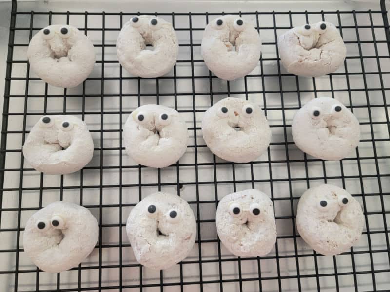 Powdered sugar donuts with candy eyes on a metal drying rack