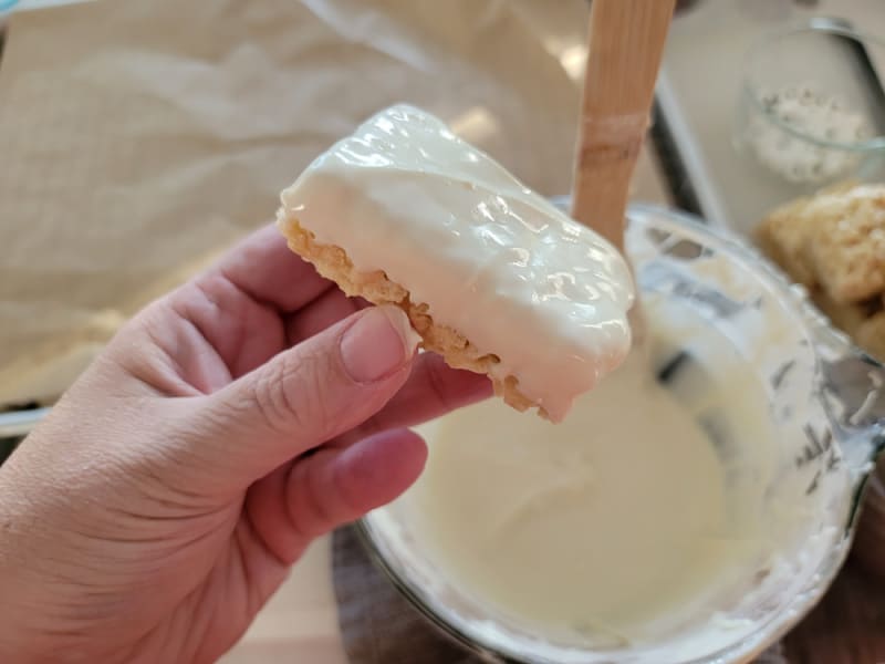 Hand holding a rice krispie treat that has been dipped in white chocolate above a bowl