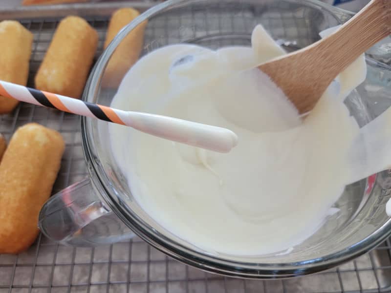 Straw dipping into a glass batter bowl filled with vanilla candy coating