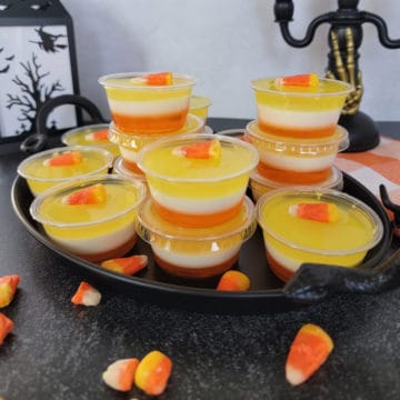 Layered Candy Corn Jello Shots on a black platter with a lantern in the background and candy corn