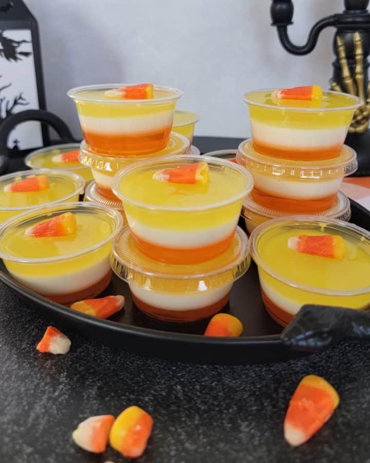 Layered Candy Corn Jello Shots on a black platter with a lantern in the background and candy corn