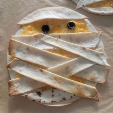 Mummy Quesadilla with black olive eyes on parchment paper