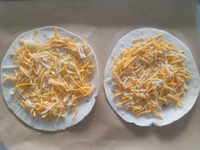 shredded cheese on tortillas on parchment paper