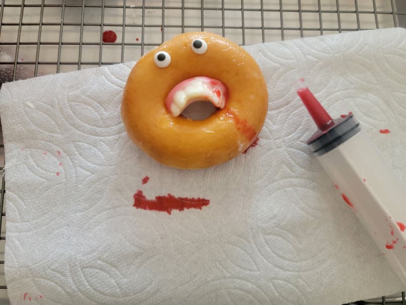 Vampire donut with fangs dripping with edible blood next to a plastic syringe 