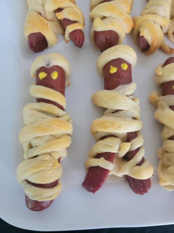 mummy hot dogs on a white plate with mustard eyes