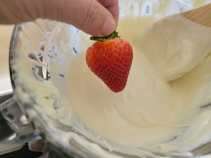 Strawberry dipping into white chocolate in a glass bowl