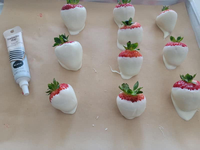 white chocolate covered strawberries on a parchment paper lined pan with an icing pen