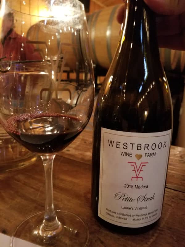 Wine glass next to a 2015 Madera Westbrook Wine Farm Petite Sirah bottle