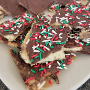 Pieces of Saltine Toffee with sprinkles on them on a white plate