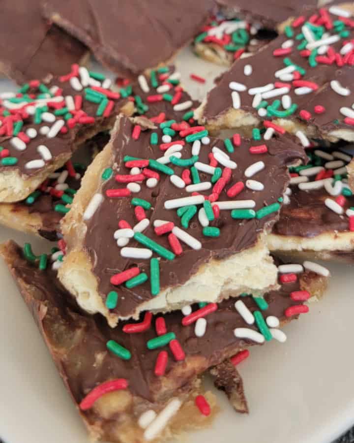 Pieces of Saltine Toffee with sprinkles on them on a white plate