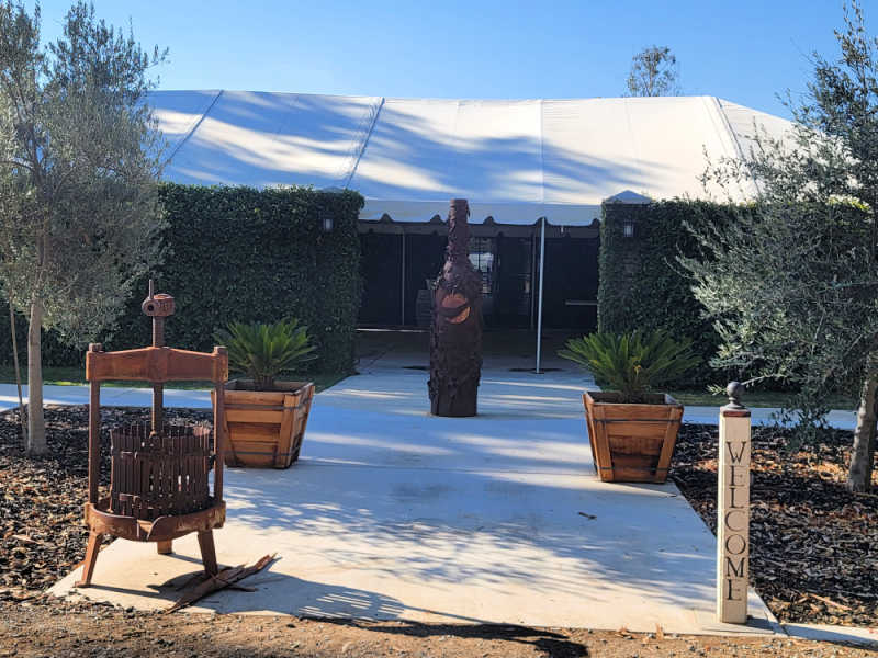 Entrance to Bird Stone Winery with a wine bottle sculpture, and grape press on a concrete pathway. 