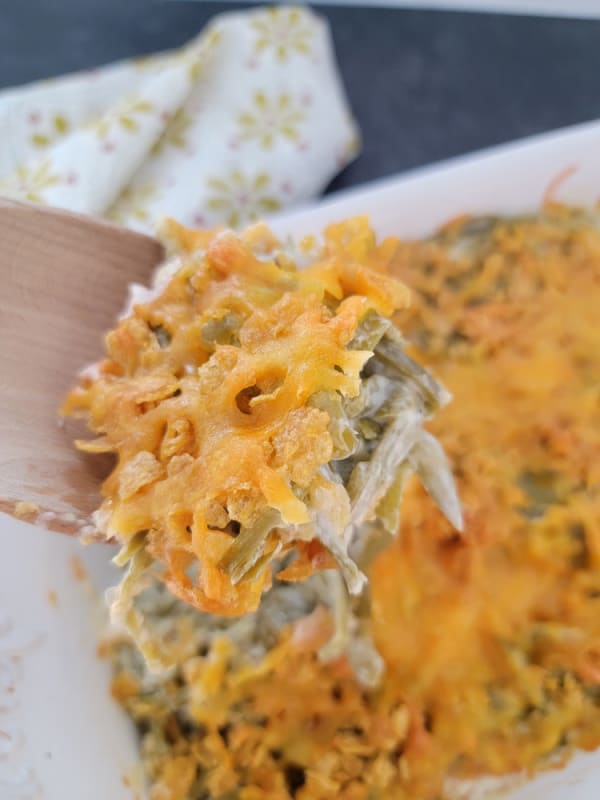 Cheesy green beans on a wooden spoon above a casserole dish