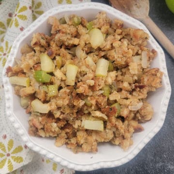 apple stuffing in a white bowl next to a cloth napkin and wooden spoon