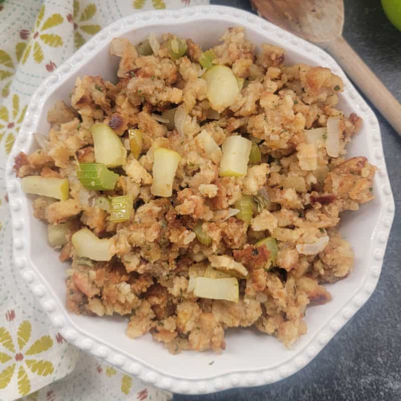 apple stuffing in a white bowl next to a cloth napkin and wooden spoon