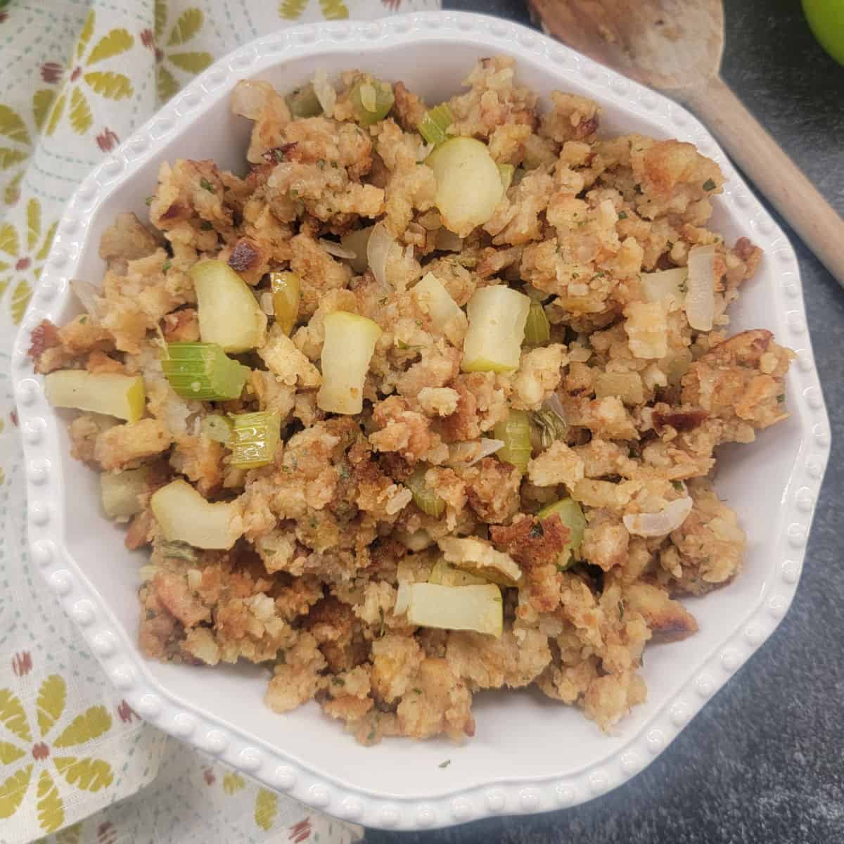 apple stuffing in a white bowl next to a cloth napkin and wooden spoon