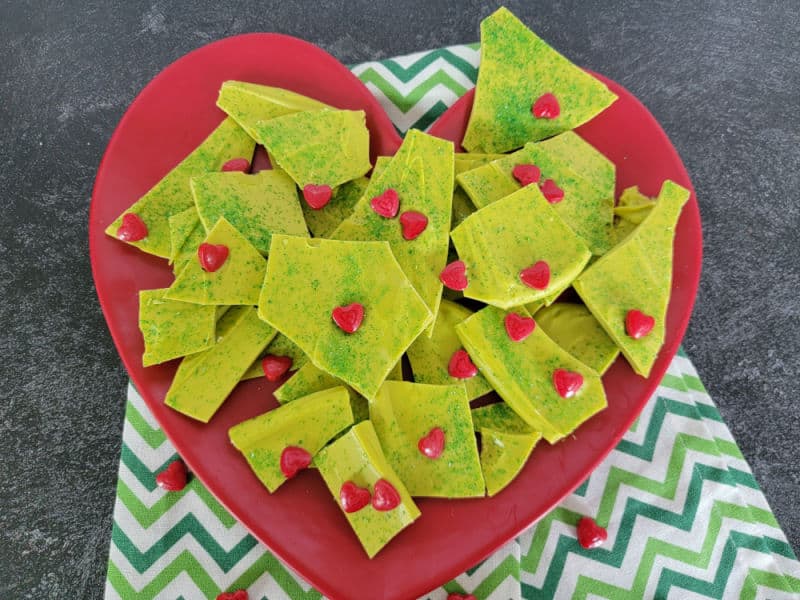 Green Grinch Bark broken in pieces with red heart candies on a red heart plate with a green chevron napkin