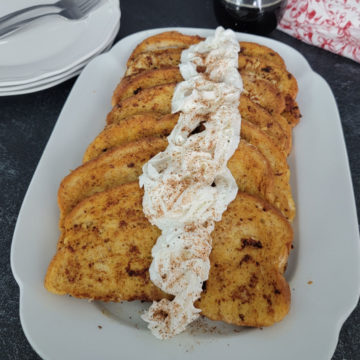 EggNog French Toast with eggnog whipped cream on a white platter next to plates