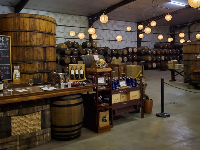 Inside Ficklin Vineyards tasting room with wine barrels stacked along the wall and wine glasses on a counter