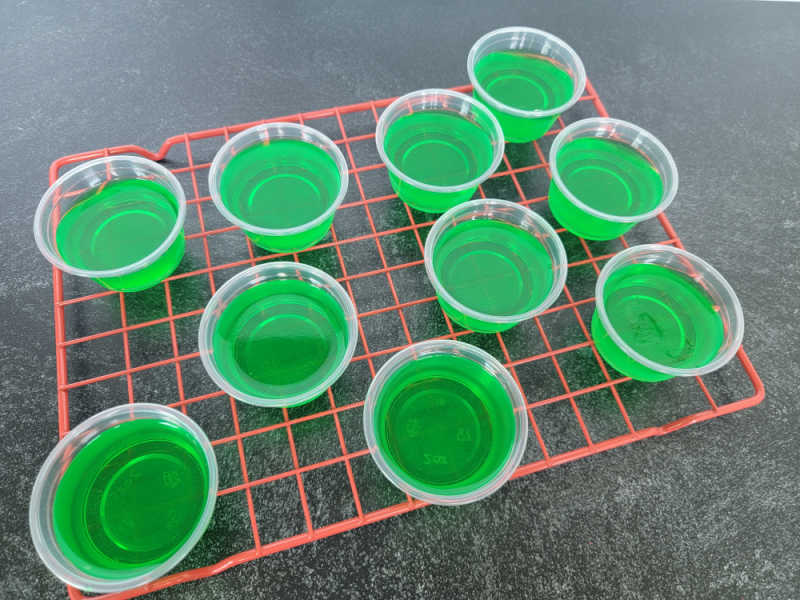 Green jello shots in plastic jello shot cups on a red cooling rack