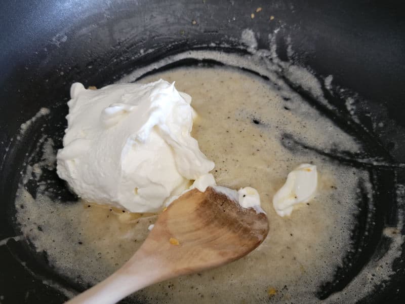 Sour cream melting in flour butter mixture for Cheesy Green Beans in a black skillet