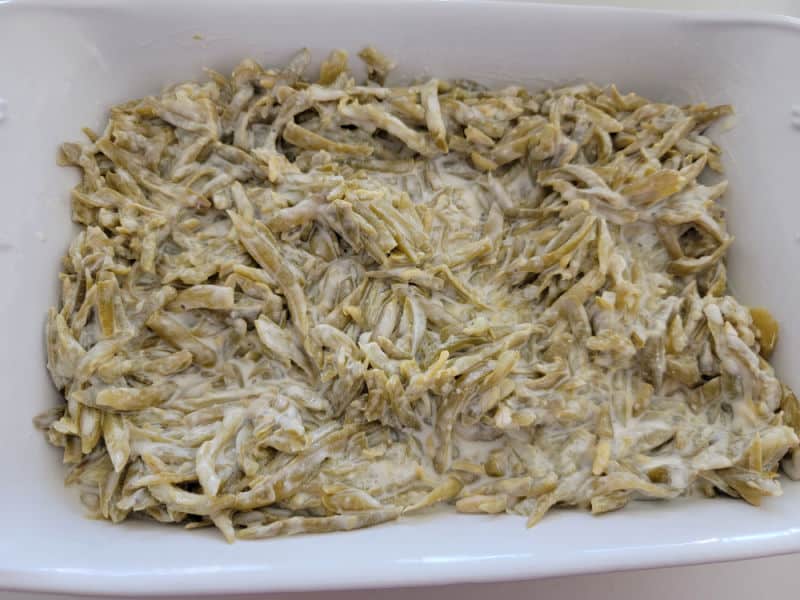 Sour cream coated green beans in a casserole dish for cheesy green bean casserole