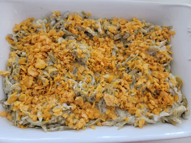 cornflake topped green beans in a white casserole dish for cheesy green bean casserole