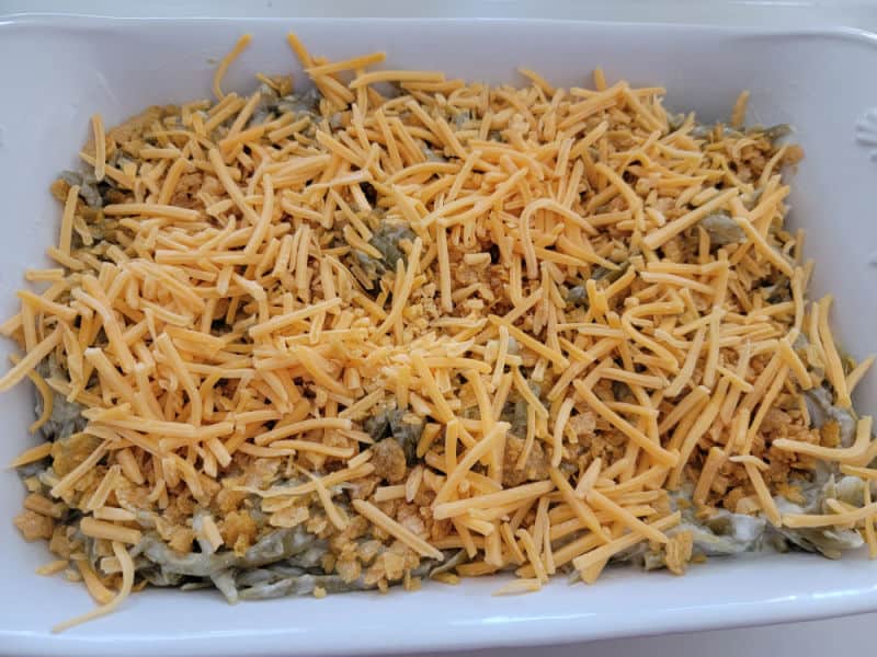 shredded cheese covered green beans in a white casserole dish for cheesy green beans recipe