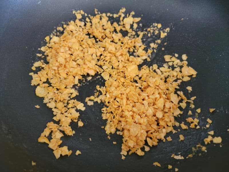 Corn flake pieces and butter in a skillet for Cheesy Green Beans