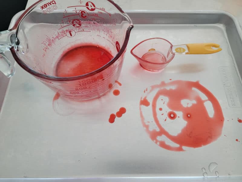 red jello stain on a baking dish with measuring cups for fireball jello shots
