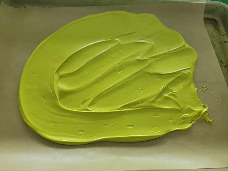 Melted Wilton Vibrant Green Candy melts spread in a oval on parchment paper