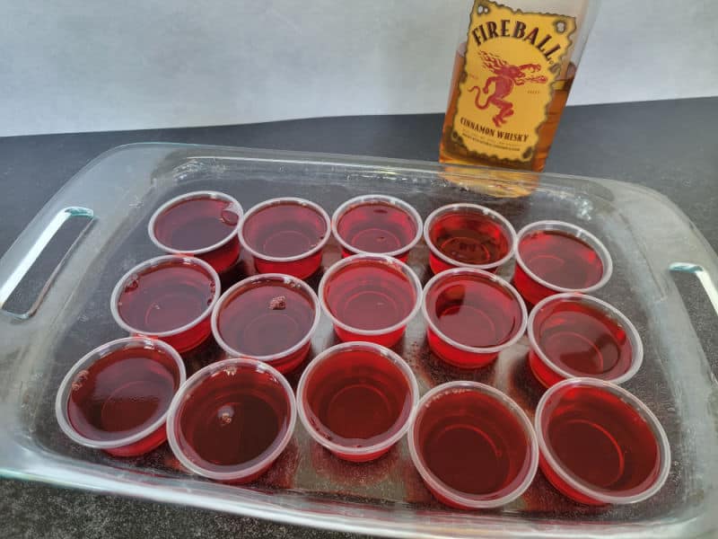 Fireball red jello shots in plastic cups in a casserole dish with a bottle of FIreball