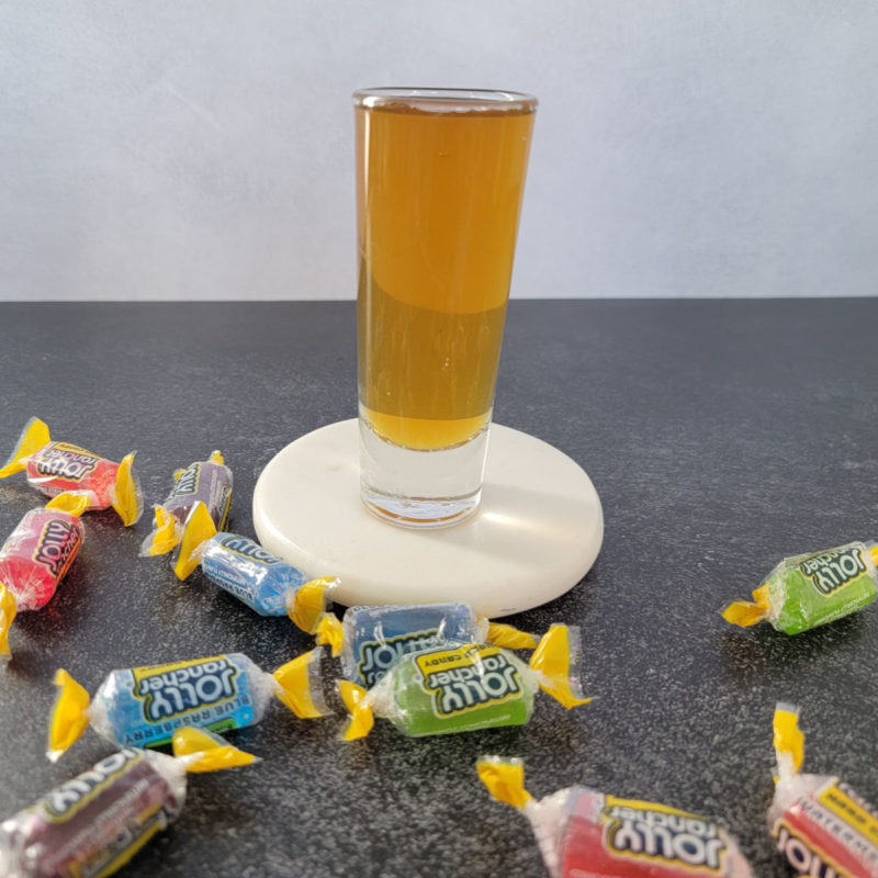 Jolly Ranch Shot on a white coaster surrounded by Jolly Rancher Candy